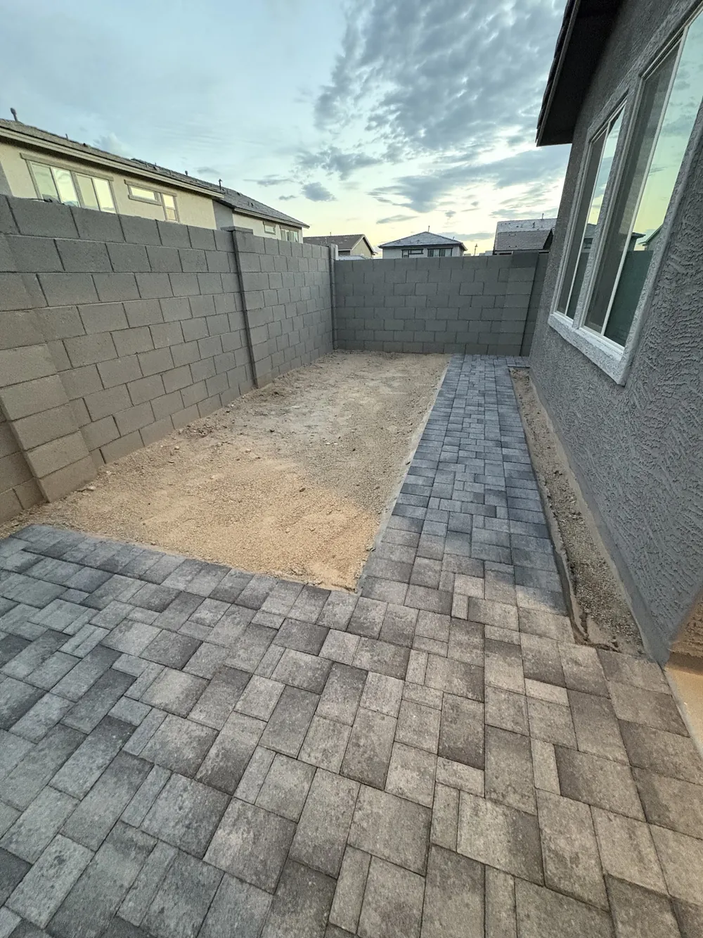 Paver walkway along the side of a gray stucco home beside a block wall, with a raked gravel bed