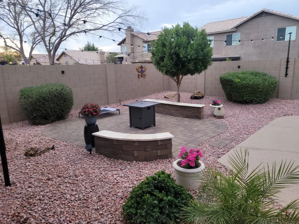 Backyard patio with a curved masonry seat wall, a fire table, a small tree and pink gravel