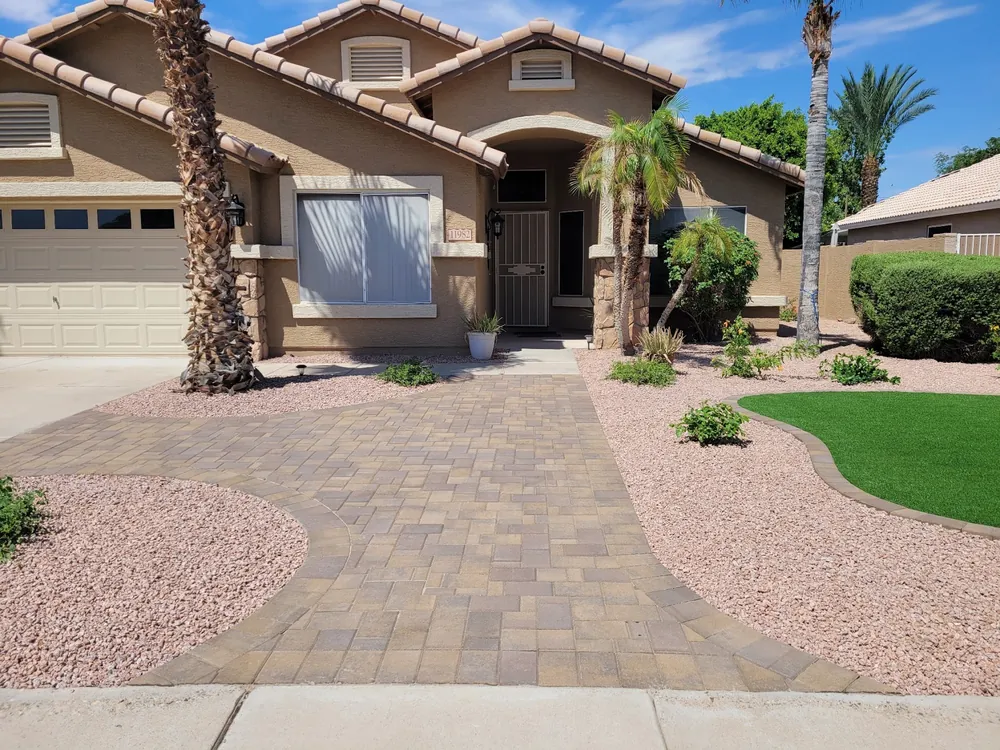 Paver driveway with curved borders and pink gravel beds in front of a tile-roof home