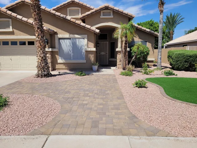 Paver driveway with curved borders and pink gravel beds in front of a tile-roof home