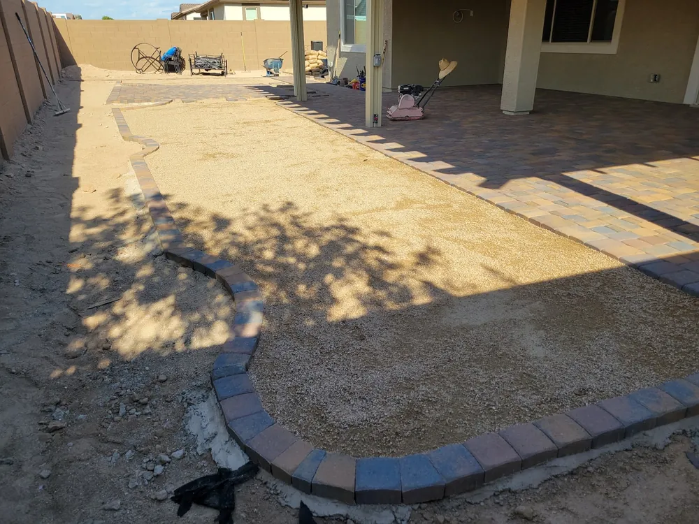 Paver border and sand base laid out for a new patio under a covered porch